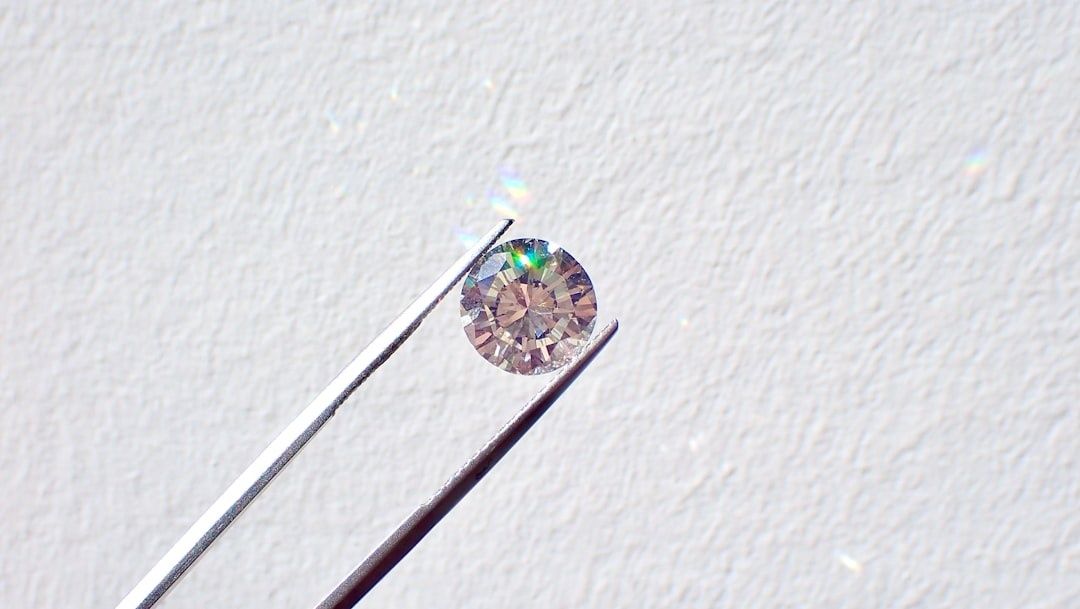 Rundslipad lös diamant som hålls med pincett mot ljus bakgrund